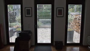 A room with three doors, each with a view of a garden through metal blinds. There is a wicker sofa and a small mat on the floor. - Junior Suite Girardi Mountain View (Sasbach am Kaiserstuhl)