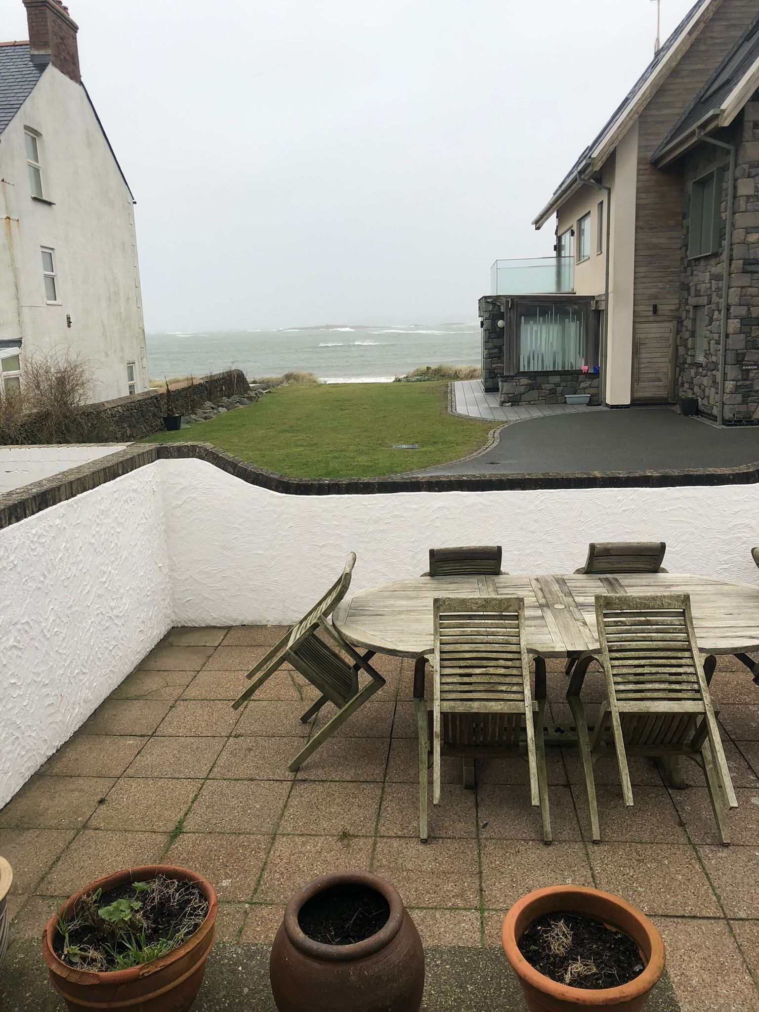 Eine Terrasse mit Tisch und Stühlen, Blick auf das Meer und ein Steinhaus.