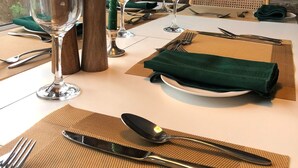 A dining table set with a green napkin, silverware, and glassware, with a rustic brick wall and a colorful painting in the background. - Bright modern holiday cottage steps from the beach and in the heart of village (Rhosneigr)