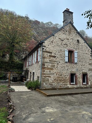 A stone building with a pitched roof, a chimney, and a small porch area.