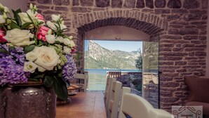 A dining area with a stone wall, a view of a lake, and a flower arrangement.