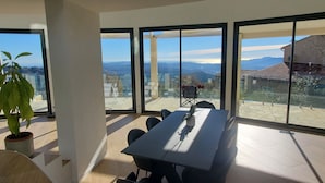 A modern dining area with a large table and chairs, large windows offering a view of the city and mountains. - South facing Villa with Panoramic Sea View, POOL, AC, Quiet  (Grasse)