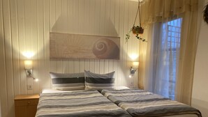Una cama bien hecha con ropa de cama a rayas, dos lámparas de noche, una obra de arte en la pared y una ventana con cortinas de gasa.