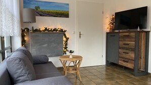 Una sala de estar con un sofá gris, un televisor de pantalla plana sobre un mueble de madera, una pared decorativa con luces y una puerta con picaporte de latón.