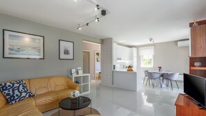 A modern living room with a sofa, a coffee table, and a TV. There is a kitchen area with a dining table and chairs. - Close to the beach, quiet location, family-friendly (Funtana)