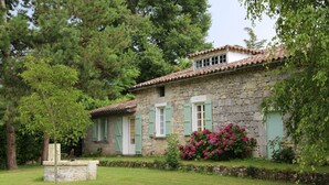 Un bâtiment en pierre avec un toit en tuiles, des volets verts et un jardin planté de fleurs.
