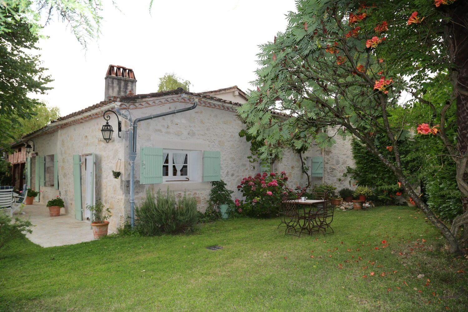 Une maison de campagne en pierre, avec un petit jardin, une table en bois et une chaise.