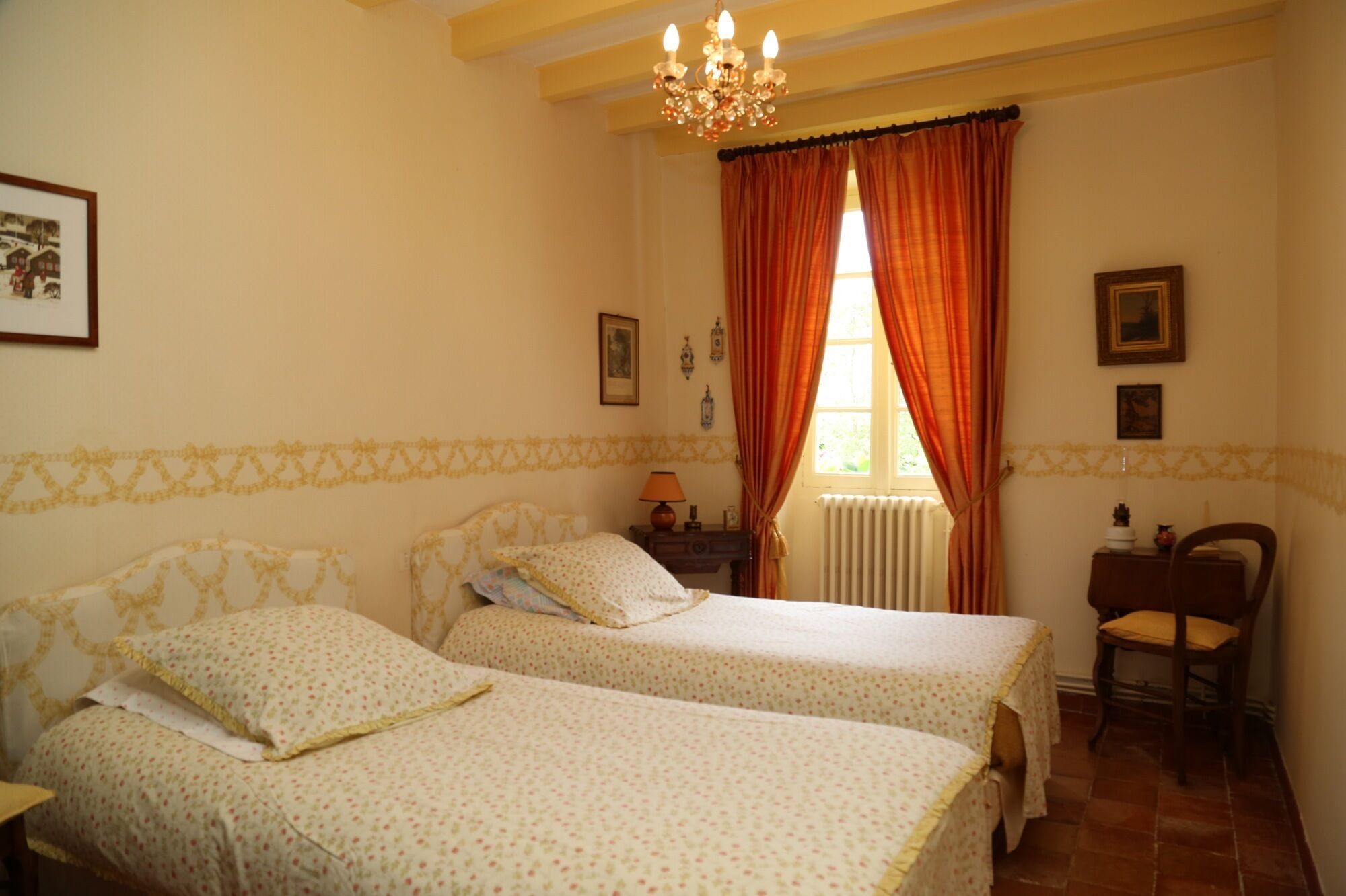 A bedroom with two beds, a chandelier, a window with curtains, and a chair.