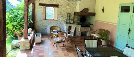 A rustic dining area with a stone wall, wooden beams, a stone fireplace, and a green door.