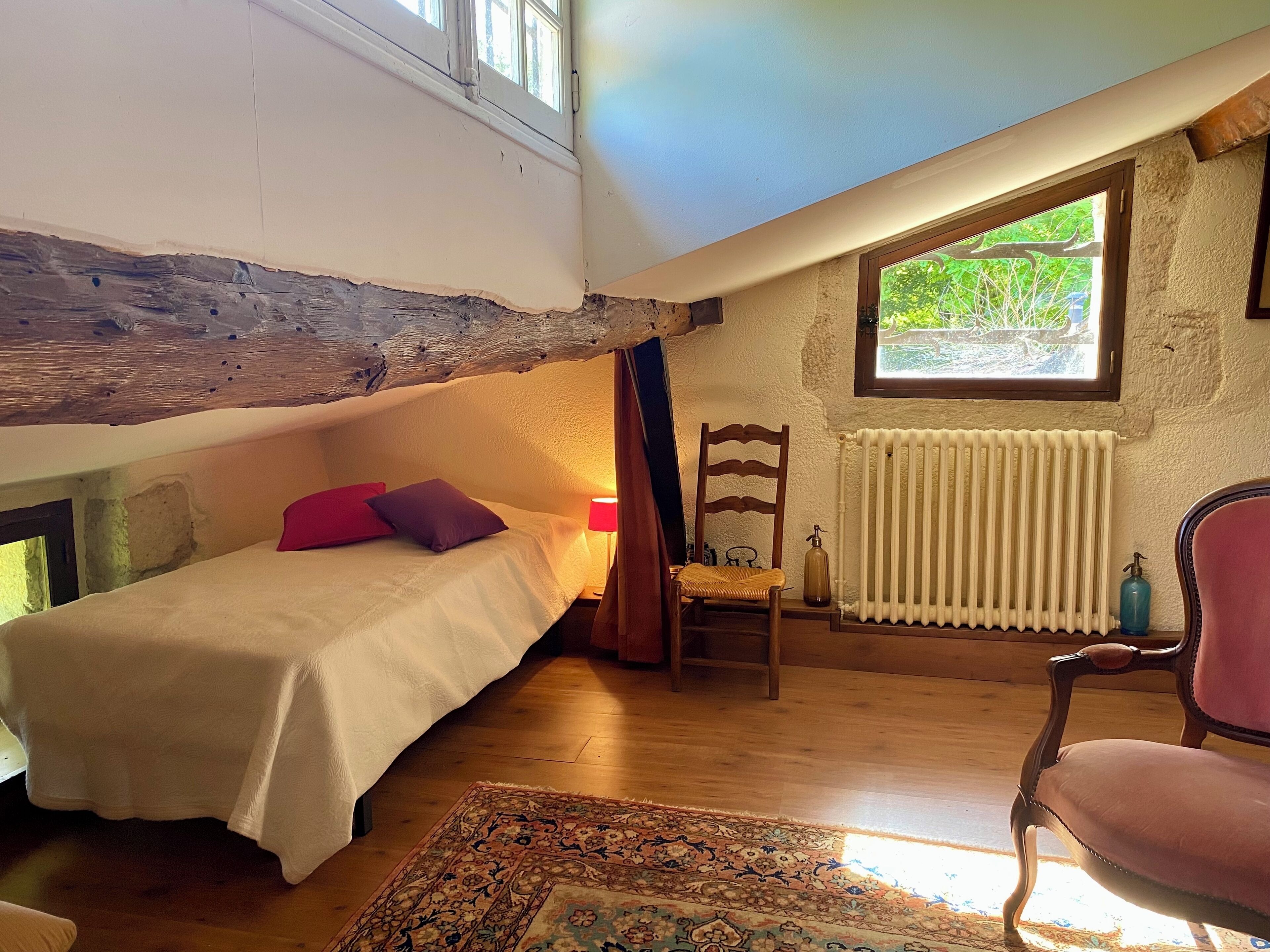 Een gezellig slaapkamer op zolder met een bed, een stoel, een radiator en een raam met uitzicht.