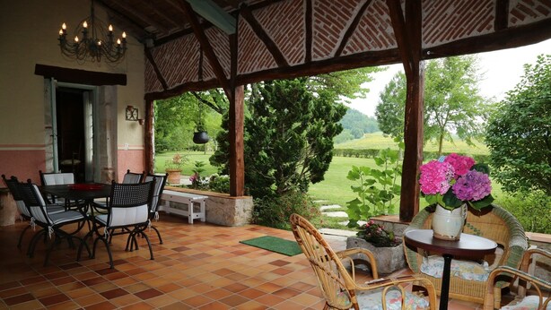 Une terrasse couverte comprenant un espace repas, des chaises en osier et une vue sur un paysage verdoyant.