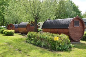 A row of wooden log cabins with a sign indicating 'Welcome, please wait.' - Stay overnight close to nature - the camping barrel (Mildenberg)