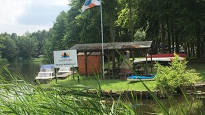 Eine Flusskabine mit einem Schild, auf dem "MARINA ALTER HAEN Herzlich Wilkommen!" steht, und einer Flagge. In der Nähe liegen Boote am Kai.