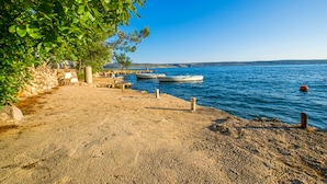 A sandy beach with boats docked, a clear blue sky, and a rocky shoreline. - Apartment near the beach with free wifi and air conditioning (Starigrad Paklenica)