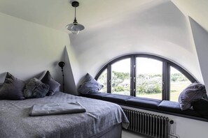 A bedroom with a large window, a bed, a radiator, and a hanging light fixture.