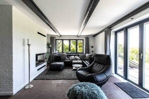 Una sala de estar moderna con chimenea, un sofá, una silla y ventanas grandes.