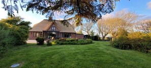 Une maison avec une pelouse bien entretenue, une façade en briques et un grand arbre au premier plan.