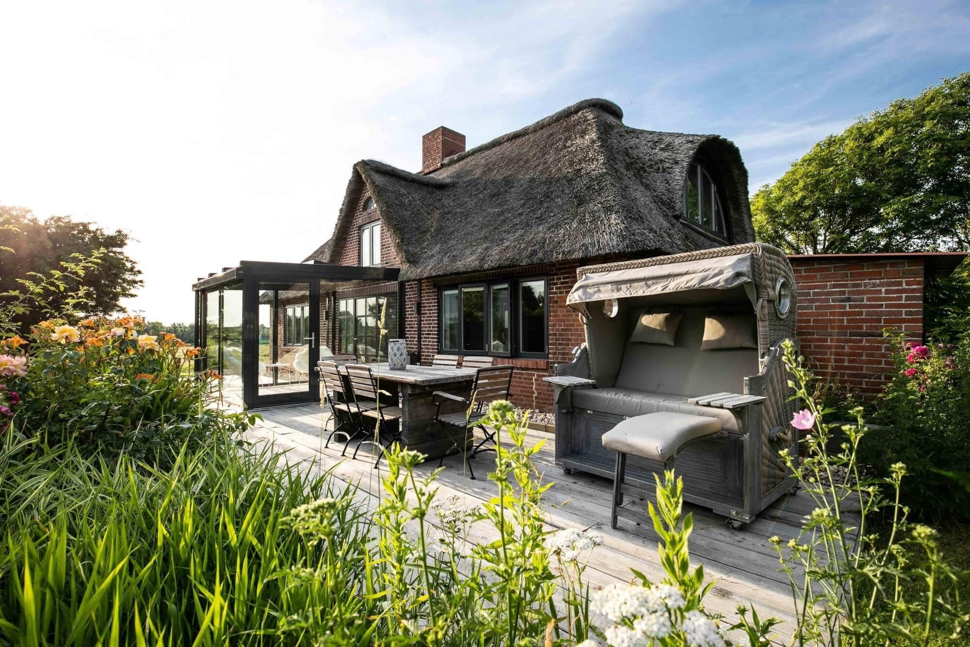 A house with a thatched roof, a patio with outdoor furniture, and a garden with flowers.