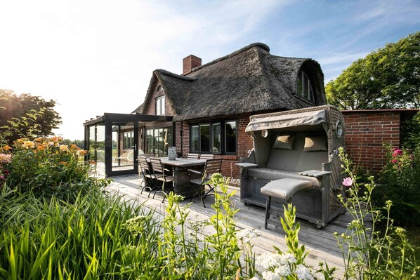 A house with a thatched roof, a patio with outdoor furniture, and a garden with flowers.