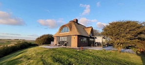 A house with a curved roof, large windows, and a grassy landscape.