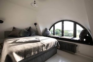 A bedroom with a bed, pillows, a radiator, and a window with a view.
