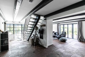 Une pièce spacieuse avec un escalier, de grandes fenêtres et un coin salon confortable.