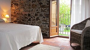Un dormitorio con pared de piedra, una cama, una silla de mimbre y vistas al exterior.