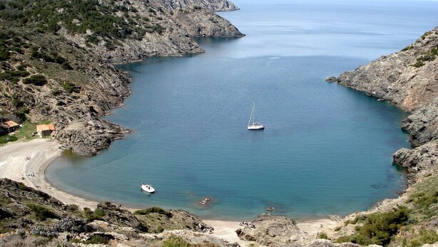 Un paisaje costero con terreno rocoso, una playa de arena y aguas tranquilas.