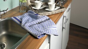 A modern kitchen with white cabinets, a stainless steel sink, a coffee maker, and two white cups on a woven tray.
