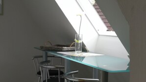 A modern dining area with a glass table and metal chairs, under a slanted skylight.