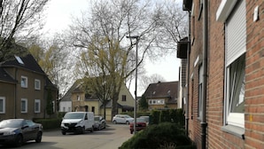 A residential street with parked cars, houses, and a brick building with a closed shutter.