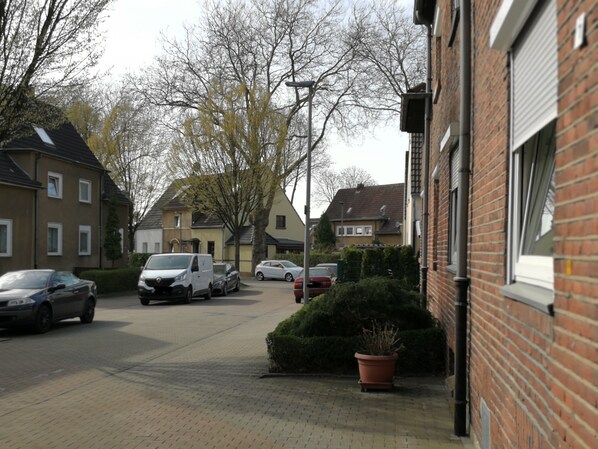 Eine Wohnstraße mit parkenden Autos, Häusern und einem Backsteinhaus mit heruntergelassener Rollläde.