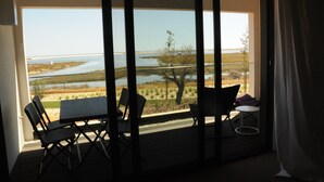 Ein Balkon mit Blick auf einen See und eine entfernte Uferlinie, ausgestattet mit zwei Stühlen und einem kleinen Tisch.