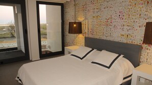 Ein Hotelzimmer mit einem großen Bett, einem Nachttisch, einer Lampe und Blick durch eine Schiebetür.