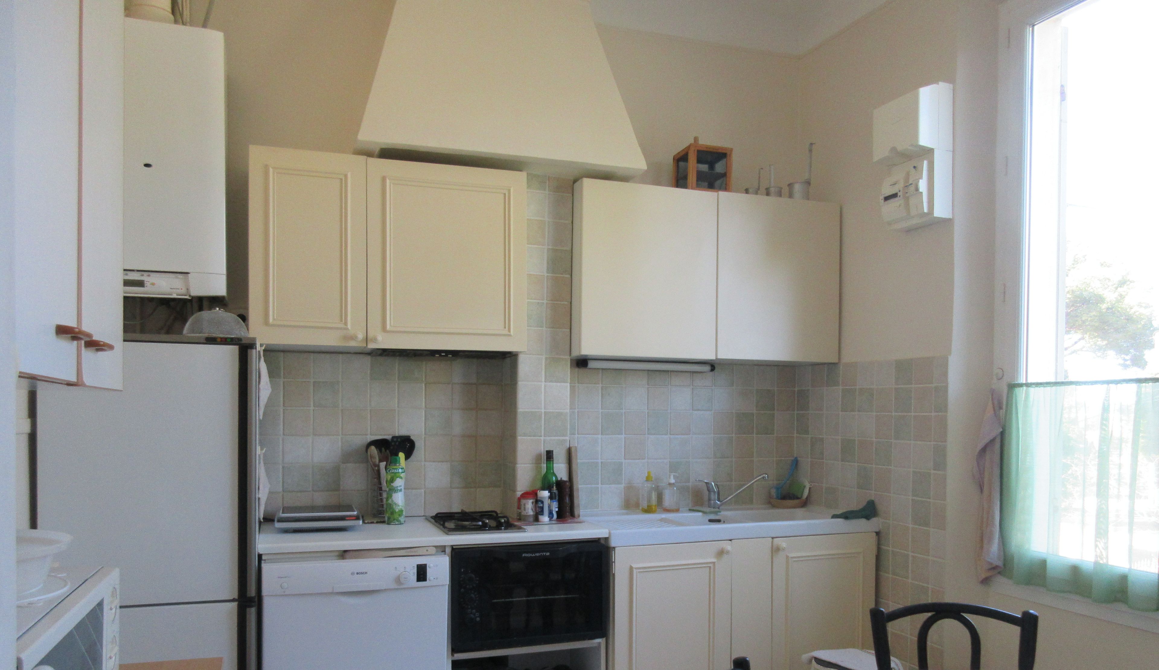 Una cocina compacta con gabinetes blancos, lavavajillas, estufa y ventana con vistas.