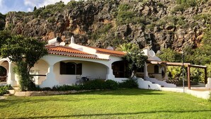 A white building with a red-tiled roof, surrounded by a well-maintained lawn and a rocky hillside. - Beautiful 10 people villa with pool on one of the most beautiful places in Albufeira (Albufeira)