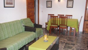 Ein Wohnzimmer mit einem grünen Sofa, einem gelben Tisch und einem Essbereich mit Holzkohlenstühlen und einer Tischdecke.