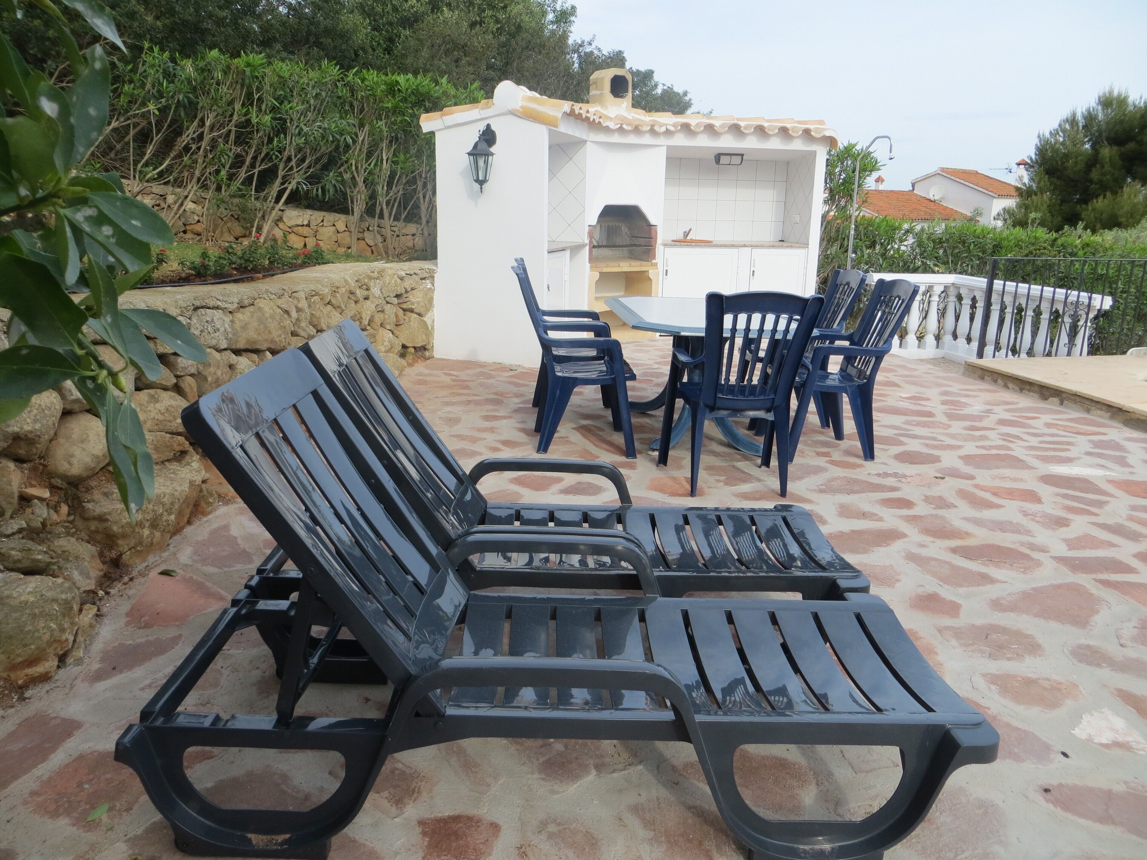 Un patio con dos sillones de descanso, una pequeña cocina exterior y suelo de baldosas de piedra.