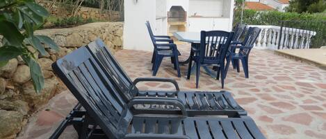 Un patio con dos sillones de descanso, una pequeña cocina exterior y suelo de baldosas de piedra.