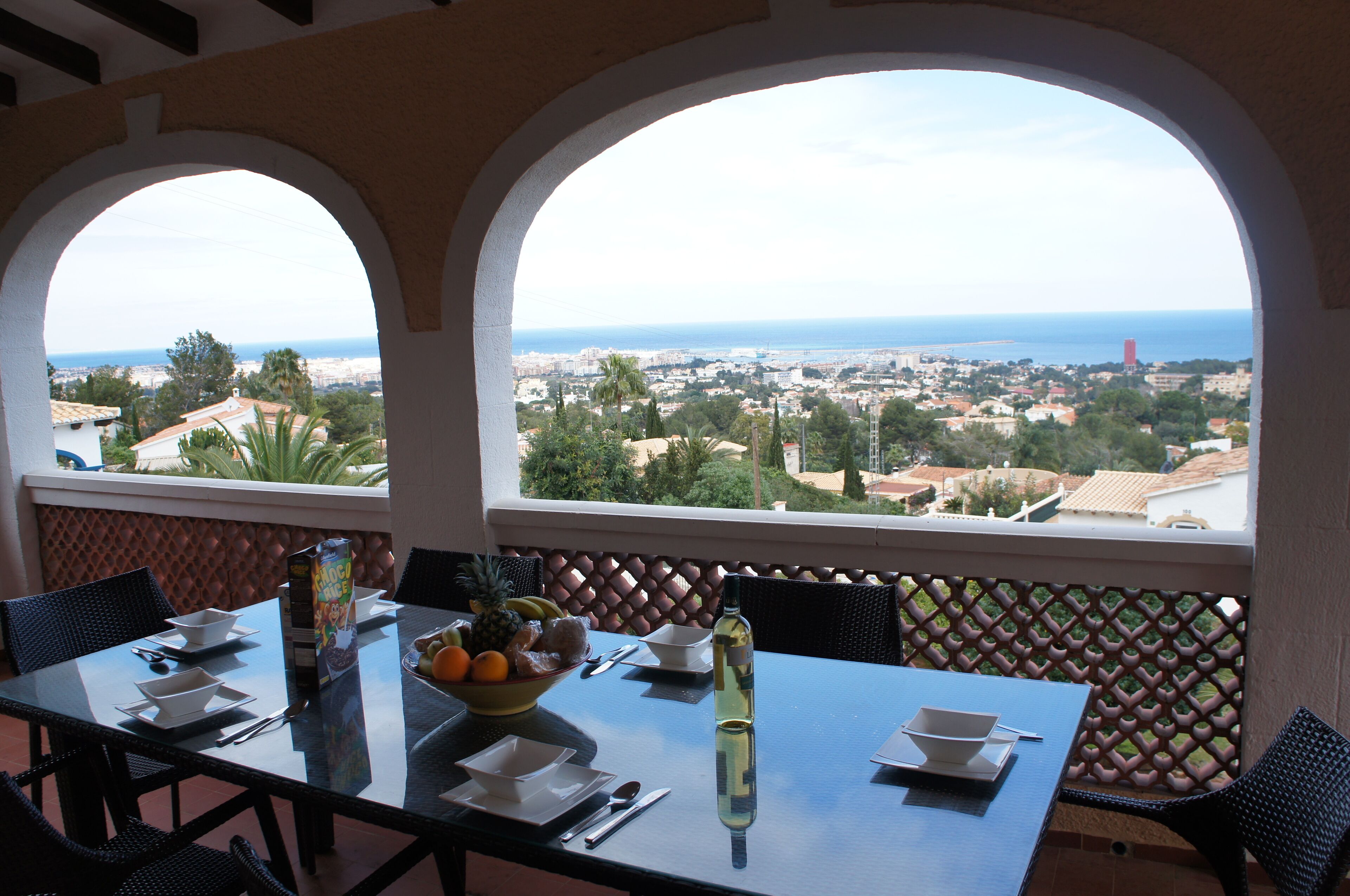 A dining table with a view of the city and sea through arched windows.