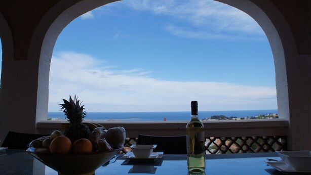 Ein Tisch mit einer Obstschale, einer Flasche und Blick auf das Meer durch ein rundbogenförmiges Fenster.