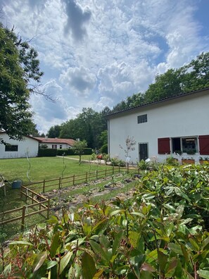A white building with red shutters, surrounded by a well-maintained lawn and garden.