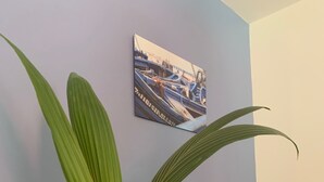 A room with a large potted plant, a sofa with cushions, and a wall-mounted picture of boats. - Apartment I" between Bordeaux and the Atlantic "Mimosa" (Brach)
