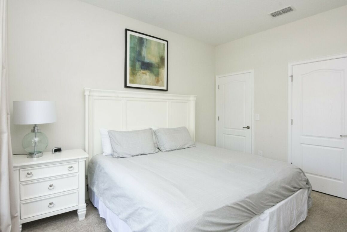 Un dormitorio con cama, mesita de noche, lámpara y puerta.