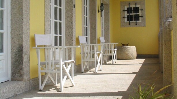 Un espace extérieur abrité, aménagé avec des chaises et des tables blanches, des murs jaunes et un pot de fleurs.