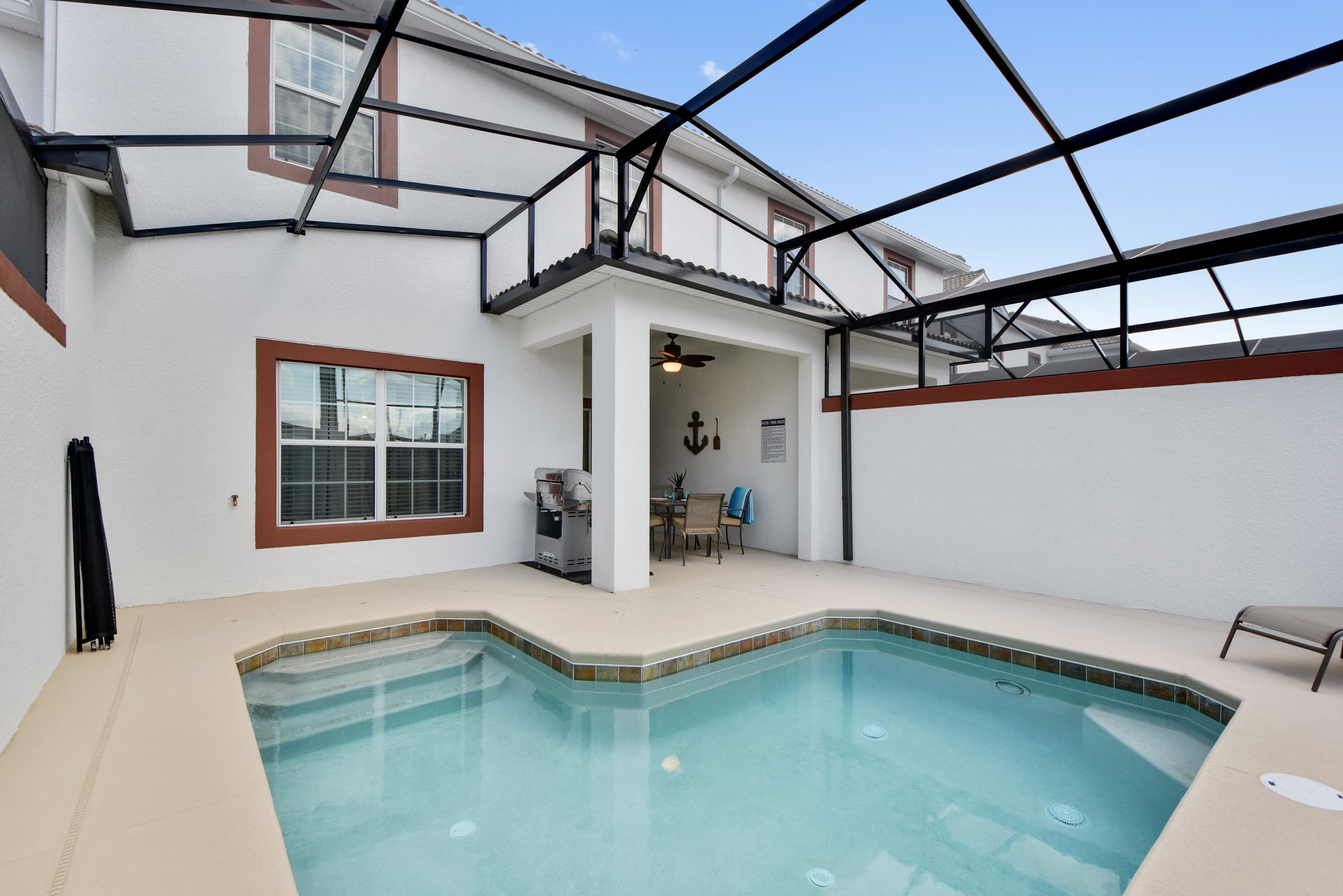 A residential swimming pool with a covered patio area, a dining table, and a ceiling fan.