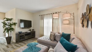 A modern living room with a sofa, a television, a large plant, and a decorative wall piece. - Charming Vacation Townhome with Pool CG1576 (Davenport)