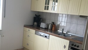Una cocina compacta con armarios de colores claros, lavavajillas integrado, estufa y fregadero.