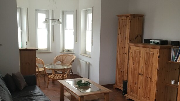 Una sala de estar con un sofá de cuero negro, una mesa de centro de madera, sillas de mimbre y un aparador de madera.