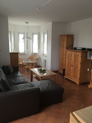 Un salon avec un canapé en cuir noir, une table basse en bois, des fauteuils en osier et un meuble en bois.
